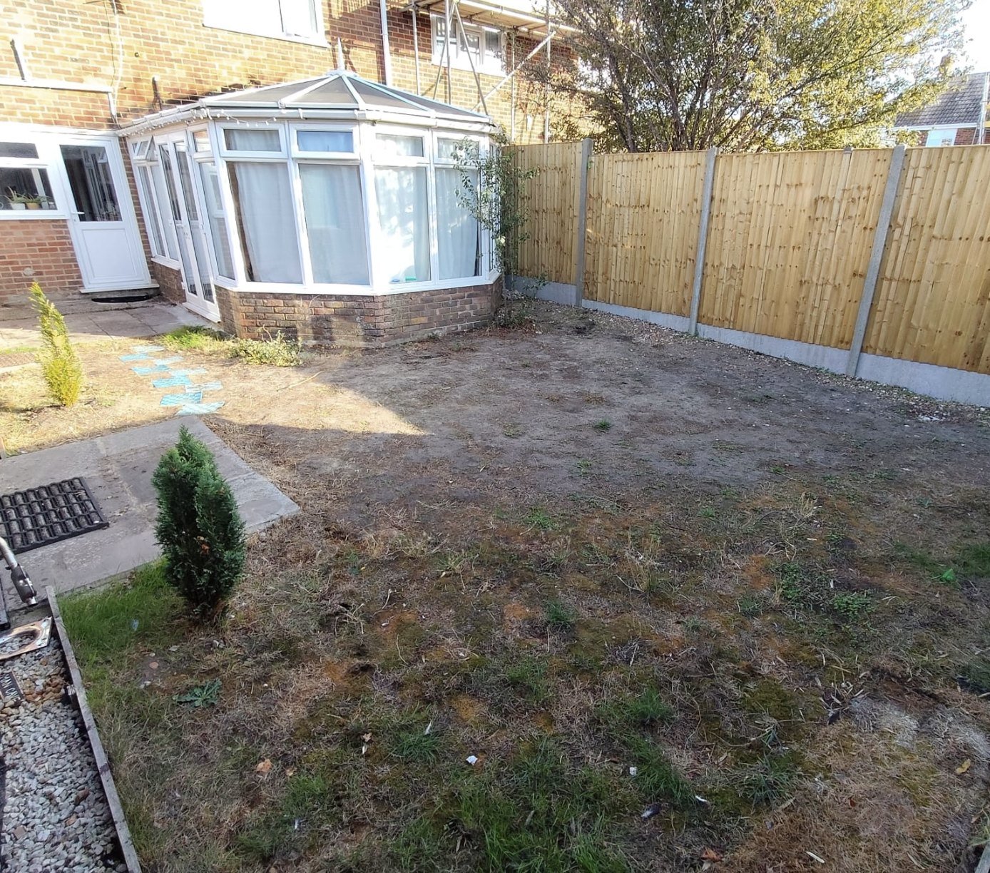 Dead patchy lawn and bare earth in front of a conservatory before new turf was laid in Lydd, Kent